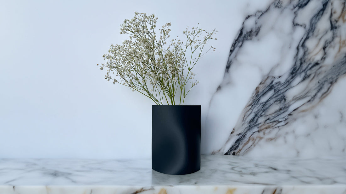 Black cylindrical vase by OBJ STUDIO holding dried flowers, placed on a marble surface, showcasing minimalist, plant-based 3D printed home décor.